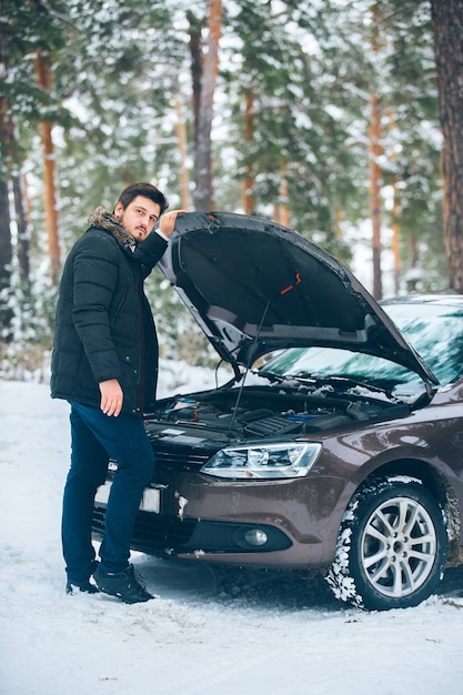 The car broke down. Beautiful young driver trying to fix the car in the woods in winter.