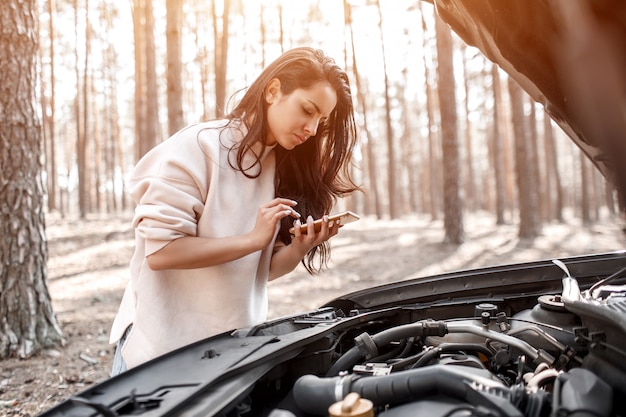 The car broke down. The woman opened the hood and checks the engine and other parts of the car.