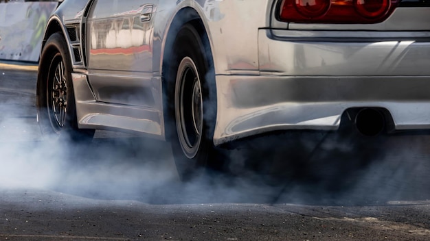 車の車輪が白い煙で燃え尽きる 車輪が燃え尽くされ 車輪が回転する時の煙が引く 車輪を引っ張る