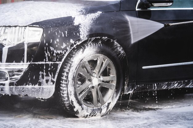 The car at the car wash is covered with foam wash under pressure with a stream of water