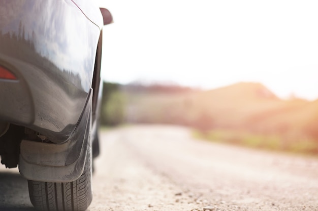 A car on a country and dusty road against a sunset background