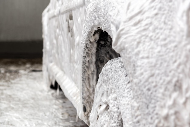 A car covered by soap foam while washing indoors closeup with selective focus