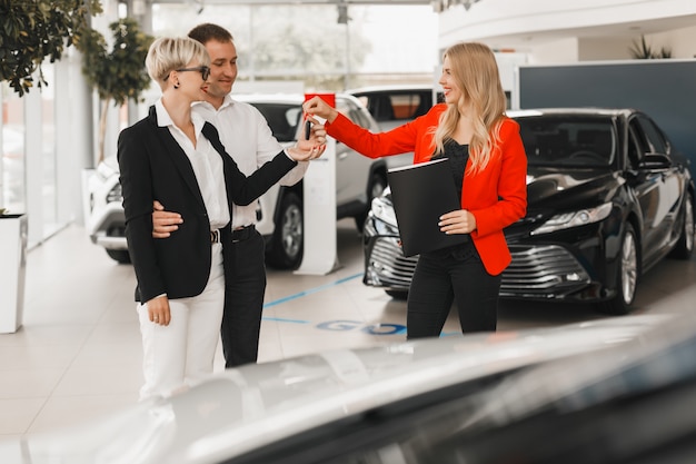 Car dealer giving key for couple  standing in car dealership.