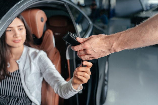 車のディーラーは若い女性に新しい車の鍵を与えています