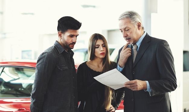 Concessionario auto leggendo un contratto per una coppia in un autosalone