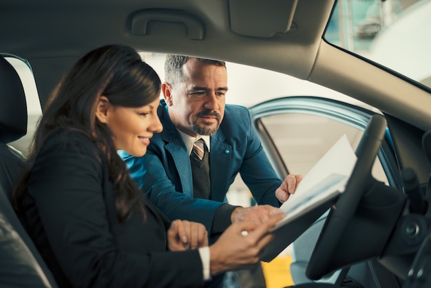 Car dealer showing businesswoman contract in car showroom.