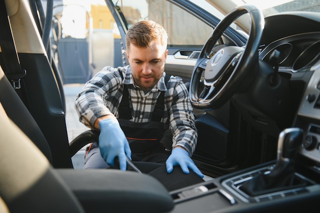 Концепция деталей автомобиля и автомойки Молодой человек, работающий в автомойке, носящий защитные резиновые перчатки, очищает интерьер автомобиля