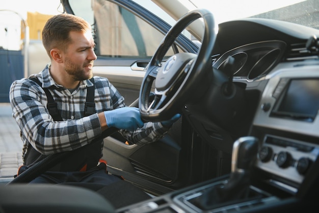 Концепция деталей автомобиля и автомойки Молодой человек, работающий в автомойке, носящий защитные резиновые перчатки, очищает интерьер автомобиля