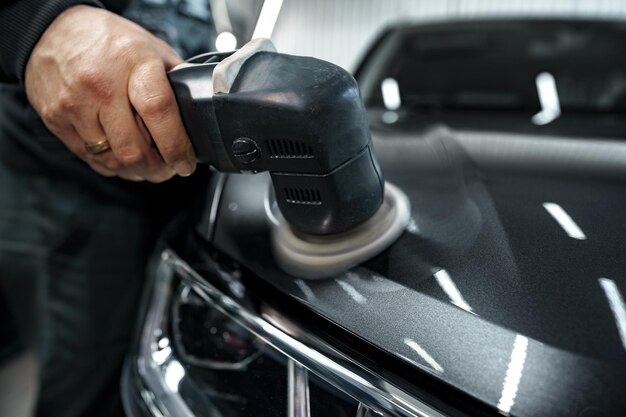 Car detailing male hands with orbital polisher in auto repair shop