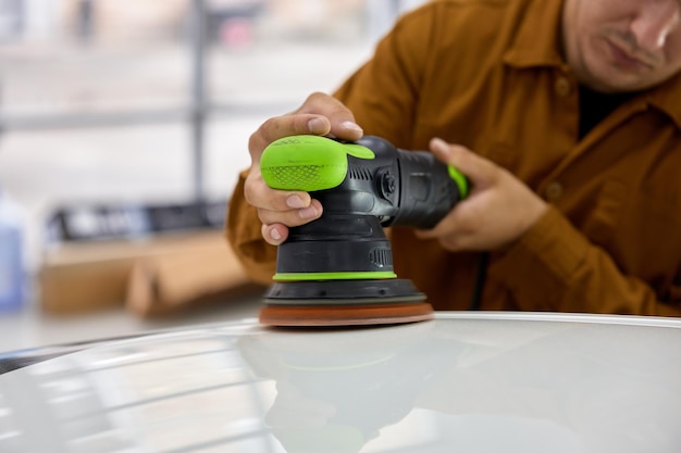 Foto concetto di dettaglio e lucidatura dell'auto. giovane che lavora con la lucidatrice orbitale prendendosi cura del tetto di un'automobile di lusso in un'officina di dettaglio