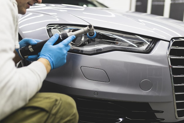 Car detailing - Worker with orbital polisher in auto repair shop. Selective focus.