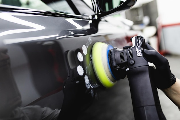 Car detailing - Worker with orbital polisher in auto repair shop. Selective focus.