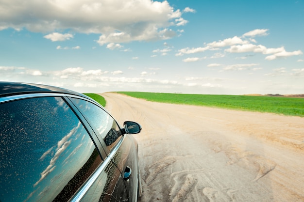 car on a dirt road and a field with green grass