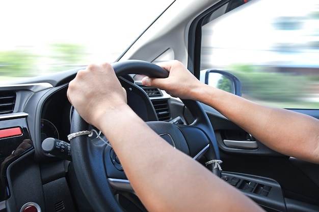 Car driver hands on the steering wheel driving a car with motion blur background.