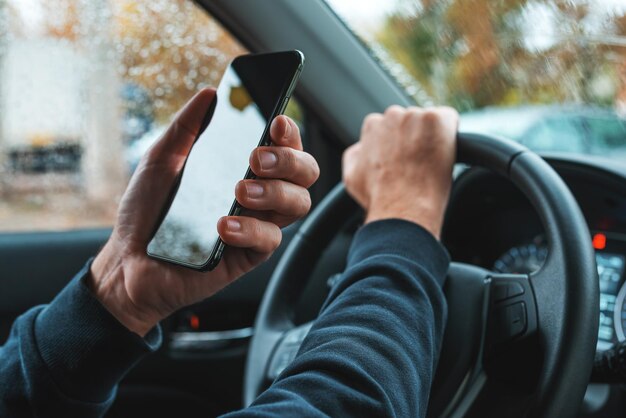 Car driver holding mobile smart phone over steering wheel blank\
black screen