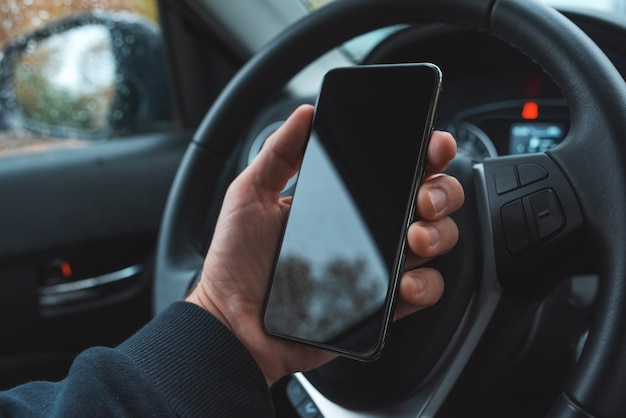 Car driver holding mobile smart phone over steering wheel blank
black screen