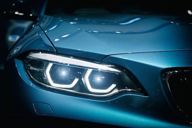 Car headlight and hood of powerful sports blue car with blue glare on dark background. 