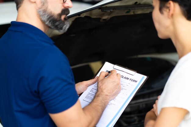 Concetto di assicurazione auto. l'agente assicurativo esamina l'auto danneggiata con le informazioni di scrittura della donna sul modulo di reclamo.