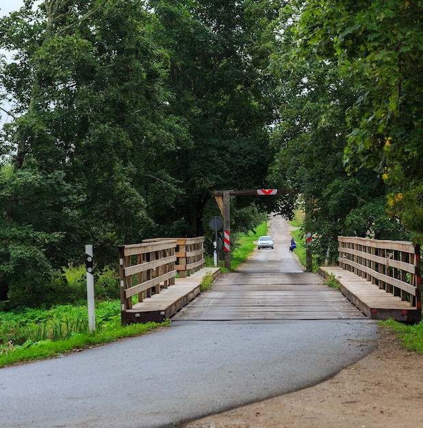 the car is driving a man is walking in the distance across the old bridge