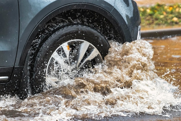 The car is driving through a puddle in heavy rain splashes of\
water from under the wheels of a car flooding and high water in the\
city