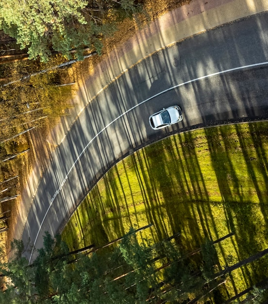 A car is driving on a winding road in the forest.