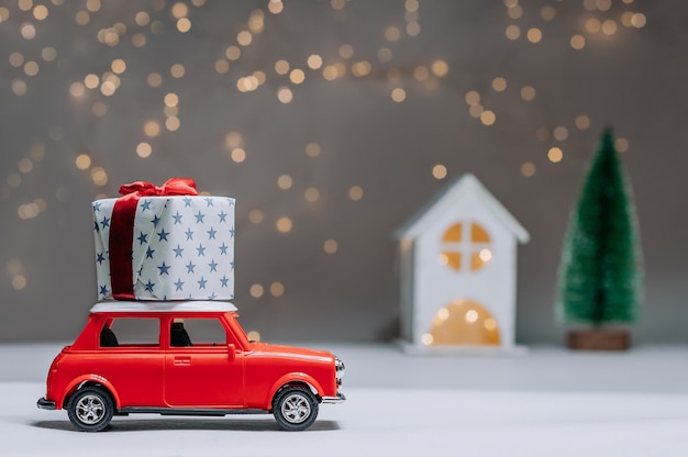 The car is taking home a big gift on the roof. against the background of a tree and lights. Concept on the theme of New Year and Christmas.