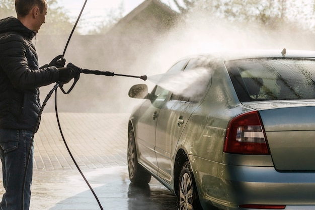 Car is washing under strong water pressure from a hose on the automatic sink backlight outside Cl