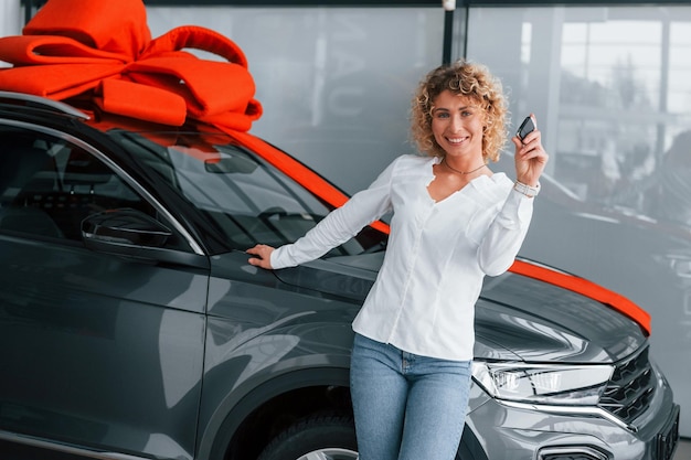 Car is with gift length on the top woman with curly blonde hair is in autosalon