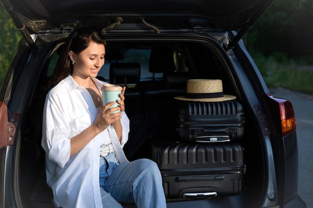 Car journey A young beautiful woman in a hat on vacation rests near the car Lifestyle