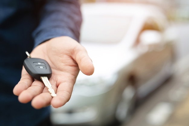 Car key, businessman handing over gives the car key to the other man on car background.