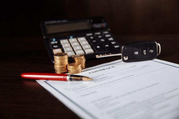 Car key and coins on contract of car purchase on wooden table.