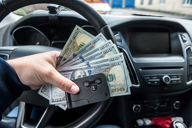 Chiave della macchina e dollaro in mano all'interno dell'auto. concetto di finanza