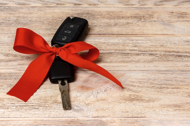 Car key with colorful bow on wooden background.