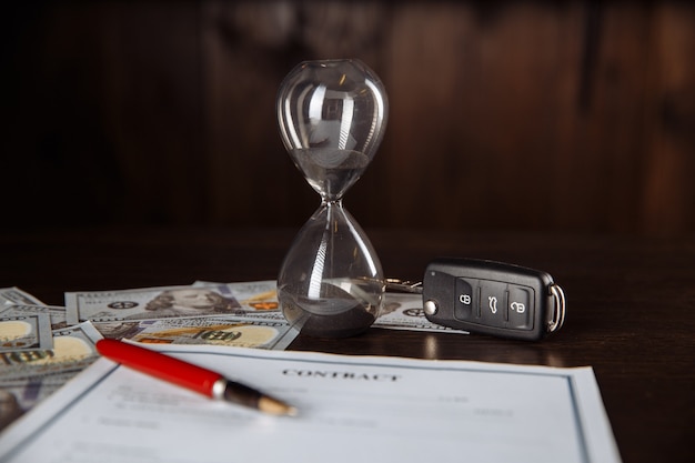 Car keys and hourglass on the signed agreement document in wooden room.