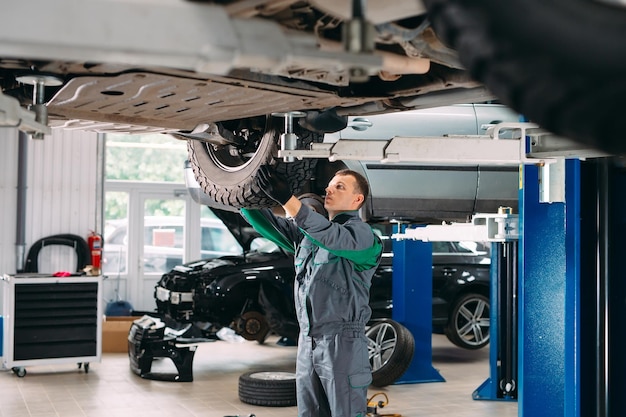 Car lifted in automobile service for fixing, worker repairs the\
wheel,