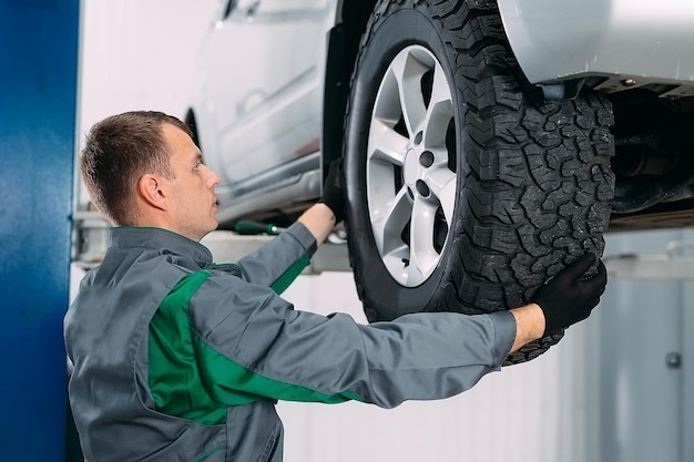 Car lifted in automobile service for fixing, worker repairs the\
wheel,