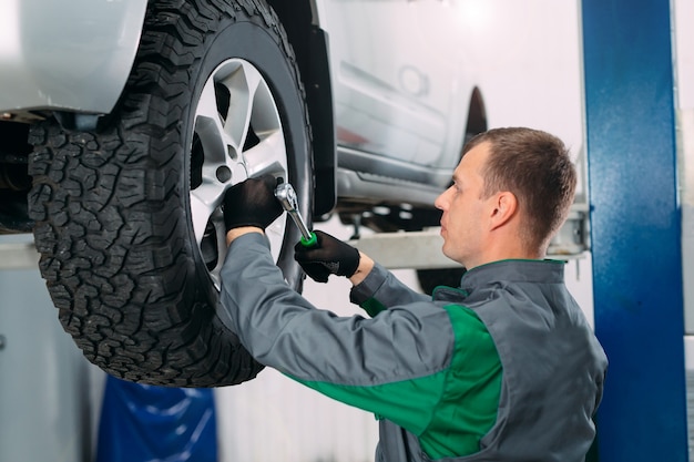 Car lifted in automobile service for fixing and worker repairs the wheel