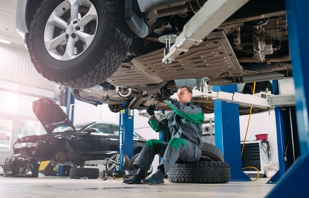 Car lifted in automobile service for fixing, worker repairs the\
wheel