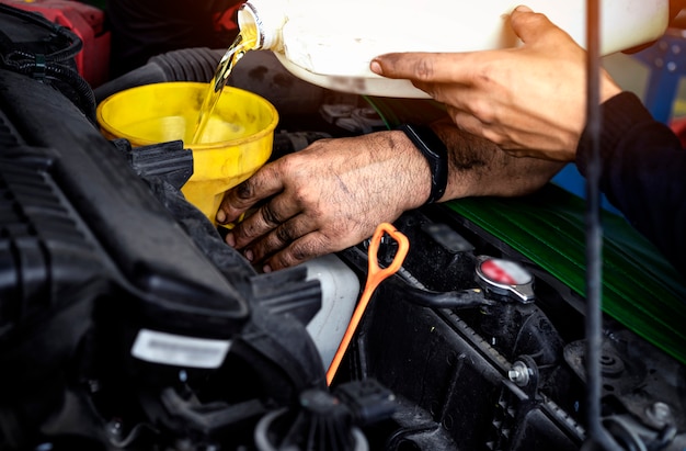 Foto concetto di manutenzione dell'automobile meccanico di automobile che sostituisce e che versa olio fresco nel motore alla stazione di servizio di manutenzione. il tecnico di riparazione automatico versa il nuovo olio per sostituire quello vecchio