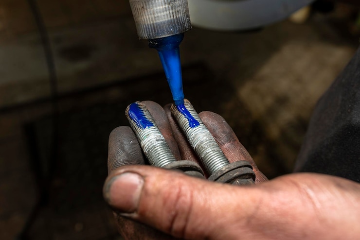 Photo car mechanic applies a layer of blue thread glue to the screw in his hand