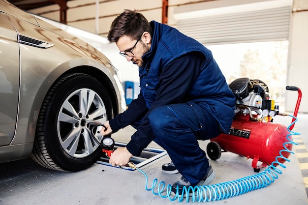 A car mechanic checking on pressure in flat tire on a car in garage