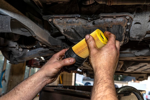 Car mechanic holding a new oil filter for a diesel engine in the background oil pan from the engine