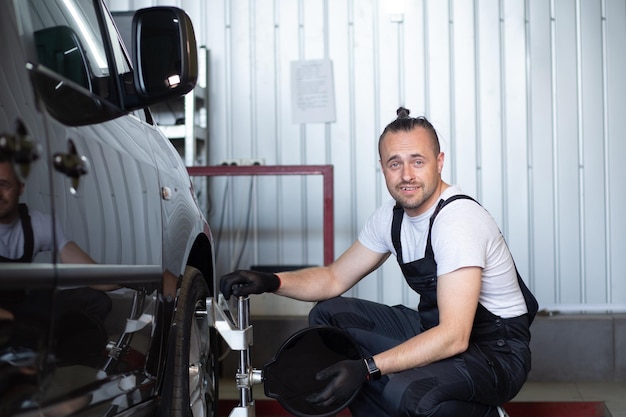 Foto meccanico automobilistico che installa il sensore durante il lavoro di regolazione delle sospensioni e di allineamento delle ruote dell'automobile presso la stazione di servizio di riparazione