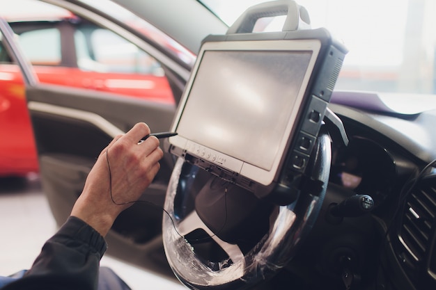 Meccanico di auto mantiene un veicolo con l'aiuto di un computer diagnostico - tecnologia moderna nell'officina riparazioni auto.