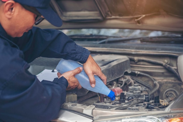 Foto meccanico auto uomo mani versando acqua distillata purificata deionizzata per servizio meccanico batteria auto close up mani uomo tenere bottiglia di acqua liquida distillata deionizzata al servizio auto mobile auto garage