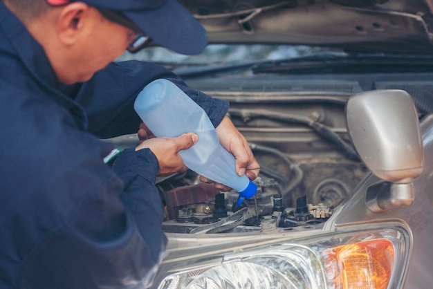 写真 車のメカニックの人が車のバッテリーの機械的サービスのために脱イオン化された精製蒸留水を注ぐ