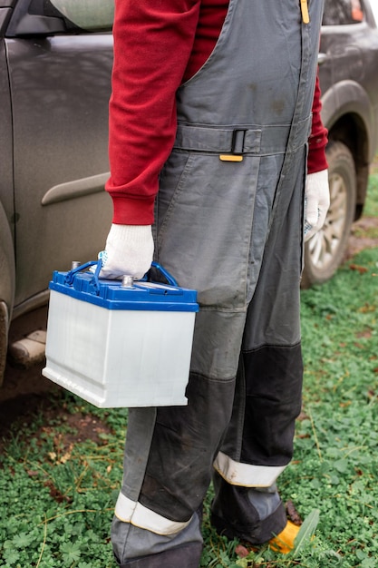 A car mechanic in overalls carries a car battery for replacement Charging and repair of accumulators