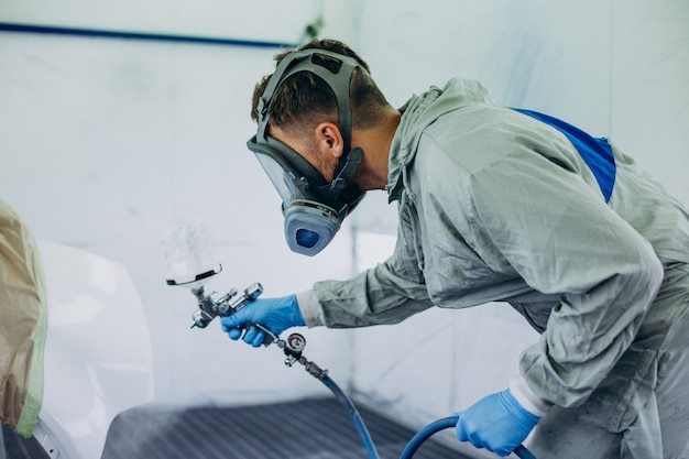 Car mechanic painting car with spray gun