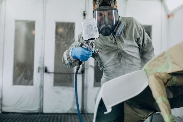 Car mechanic painting car with spray gun