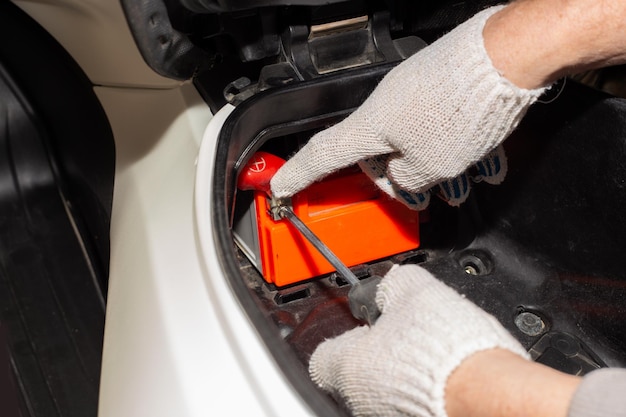 The car mechanic removes the battery from the motorbike. Battery repair and replacement.